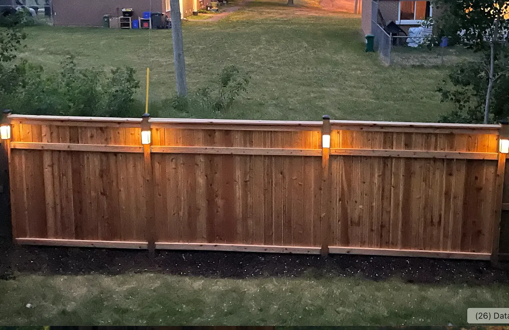 Cedar privacy fence with cap rail and warm post lighting at dusk in an Ottawa backyard