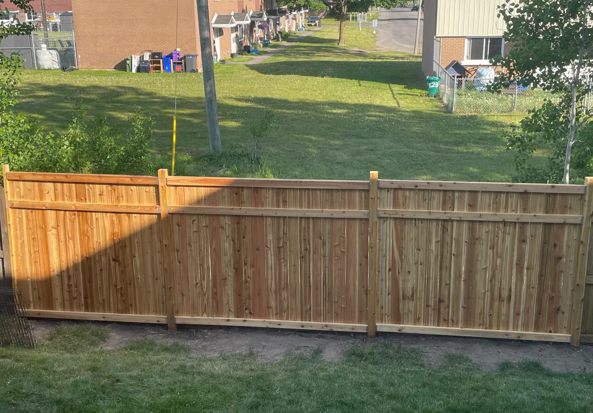 Daytime view of the same cedar privacy fence with cap and trim boards along the property line
