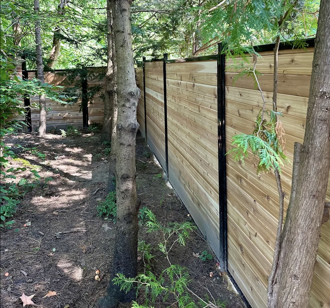Second view of the horizontal cedar fence weaving between mature trees in an Ottawa backyard