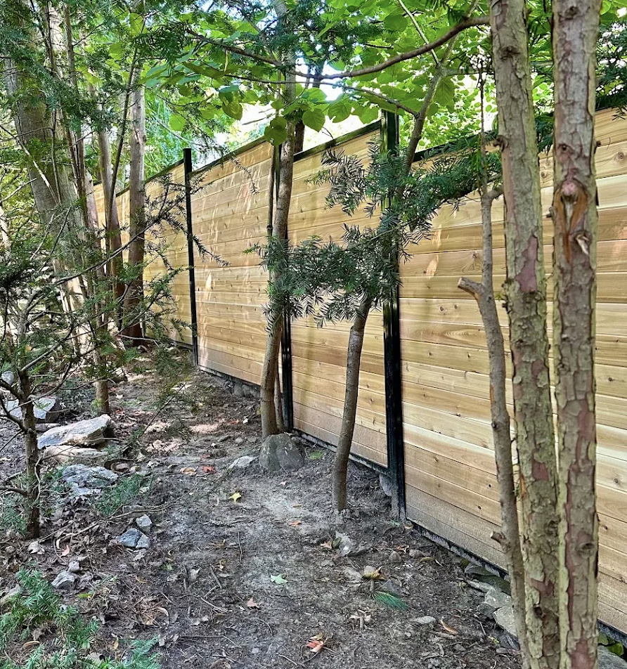 Hybrid horizontal western red cedar fence with black steel posts installed on a treed, sloped Ottawa property