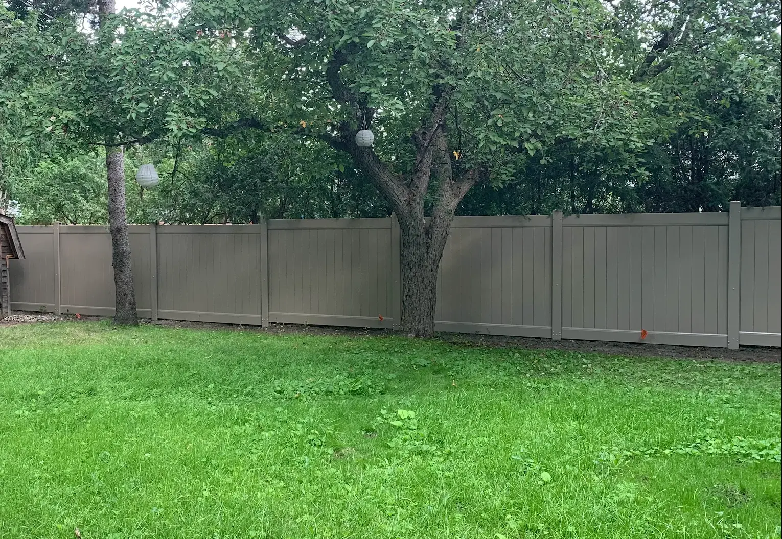 Taupe vinyl privacy fence running along a tree-lined Ottawa backyard with open lawn