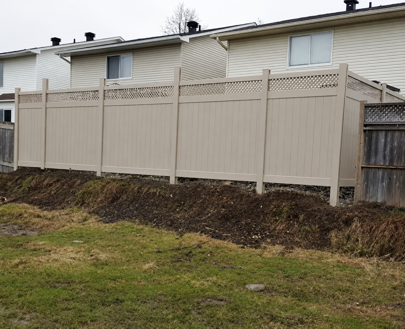 Tan PVC privacy fence with lattice top installed along a raised grade in an Ottawa backyard